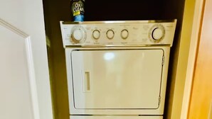 A compact laundry room with a stacked washer and dryer, a door, and a tiled floor. - Ski & Golf Getaway Suite - private hot tub - 2 bed (Kimberley)