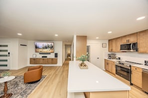 A modern kitchen with wooden cabinets, a central island, and a flat-screen TV mounted above the island.