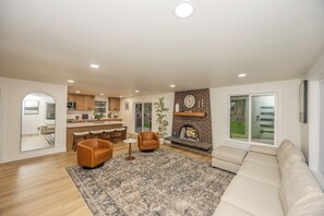 A modern living room with a fireplace, a sofa, and a dining area with bar stools.