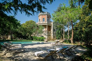 Ein Poolbereich mit Liegestühlen und ein Steinhaus mit Balkon.
