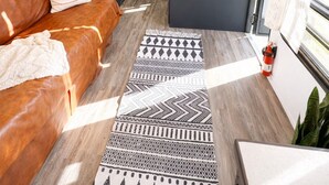 A compact RV interior with a kitchenette, a brown leather couch, and a patterned rug.