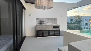 A modern balcony with a concrete bench, a hanging light fixture, and a view of buildings in the background. - Jungle Vibes Studio in Tulum / Private (Tulum)