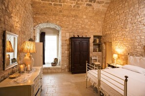 A stone-walled room with a bed, a dresser, a mirror, and a window with a view. - Masseria Le Cerase – An Apulian Masseria for 10 People (Conversano)