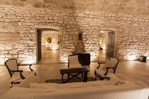 Una habitación con paredes de piedra, una chimenea, zona de estar y vistas a través de un arco.