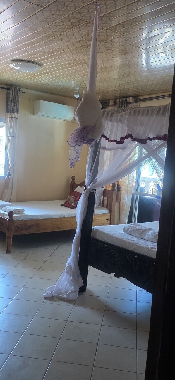 A room with two beds, a ceiling fan, an air conditioning unit, and a window with curtains.