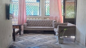A room with a patterned rug, a sofa, a chair, and a potted plant. - Luxurious 4-bedroom Holiday House With Pool Access in Diani Beach (Diani Beach)