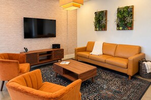 A modern living room with a flat-screen TV, a sofa, two armchairs, a coffee table, and a decorative plant wall. - Rooftop views | Sleeps 14 | Walk to the stadium (Austin)