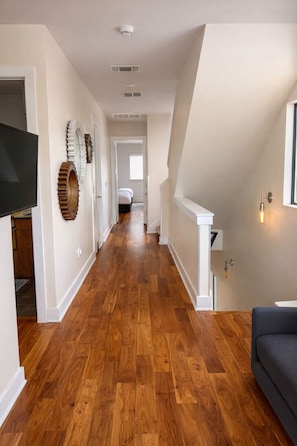 A hallway with wooden flooring, white walls, a flat-screen TV, decorative wall art, and a staircase. - Rooftop views | Sleeps 14 | Walk to the stadium (Austin)