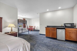 Une chambre d’hôtel comprenant un lit, un bureau avec une lampe, une kitchenette équipée d’un four à micro-ondes et donnant sur l’extérieur.