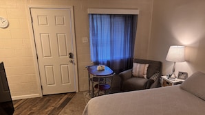 Ett hotellrum med en säng, ett litet bord med en stol, en lampa och en klocka på väggen.