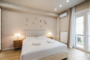 A hotel room with a large bed, two bedside tables with lamps, a ceiling light, a wall-mounted air conditioner, and a sliding glass door to the outside. - Acropolis Propylaea Apartment by A&A Residencies  (Athens)