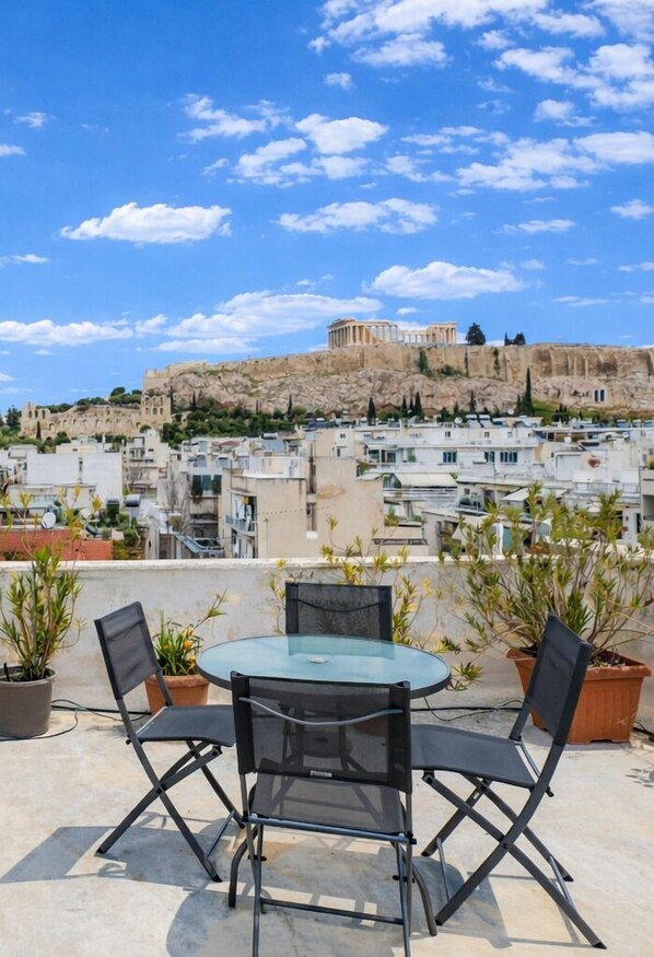 A rooftop terrace with a glass table and chairs, overlooking a cityscape with historic buildings and a hill. - Acropolis Propylaea Apartment by A&A Residencies  (Athens)