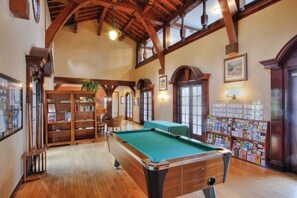 A pool table in a room with wooden beams, bookshelves, and a fireplace.
