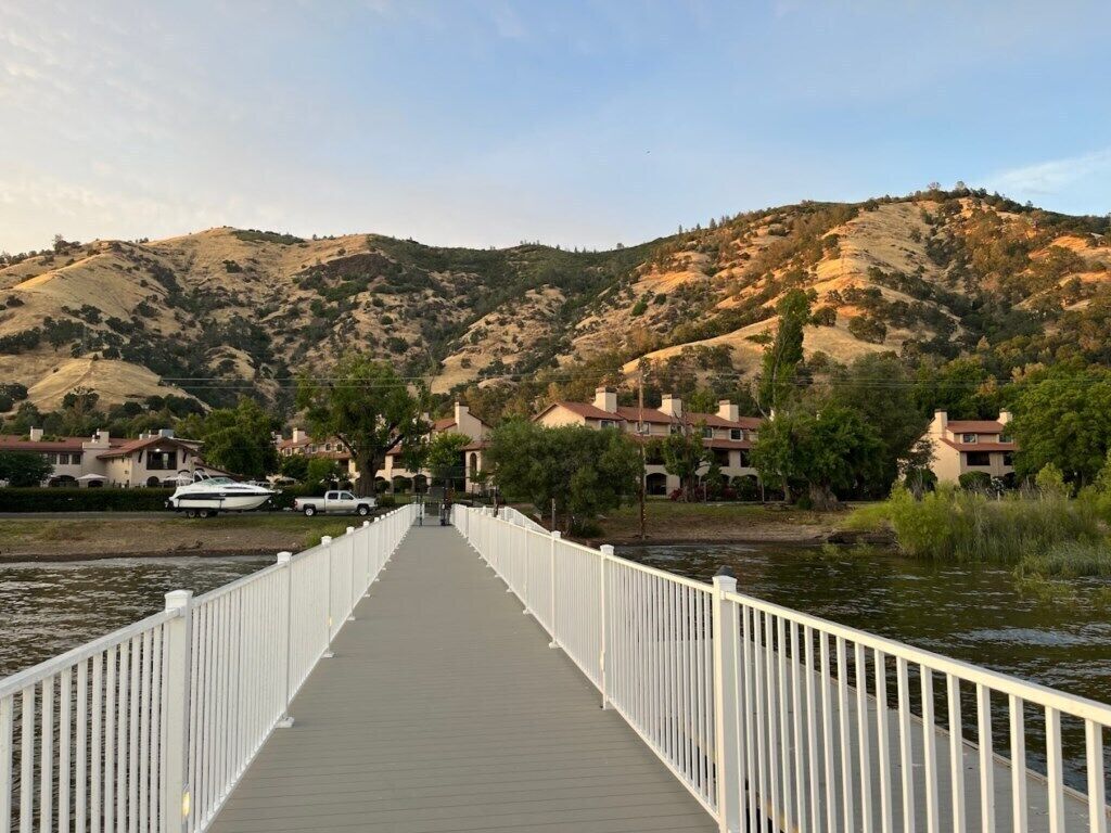 A wooden boardwalk leading to a body of water with hills in the background.