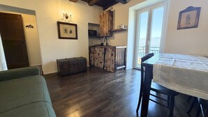 A living room with a sofa, a dining table with chairs, a kitchen area with wooden cabinets, and a sliding glass door leading to a balcony. - Enchantment of the Lake app Menaggio two-room apartment with bathroom and balcony (Molina)