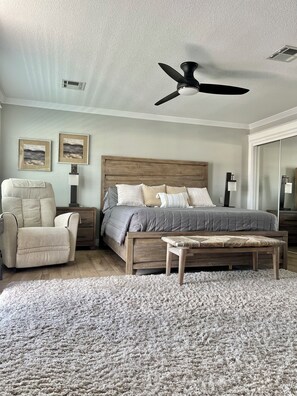 Ein Schlafzimmer mit Bett, Sessel, Nachttisch, Stehlampe und Deckenventilator.