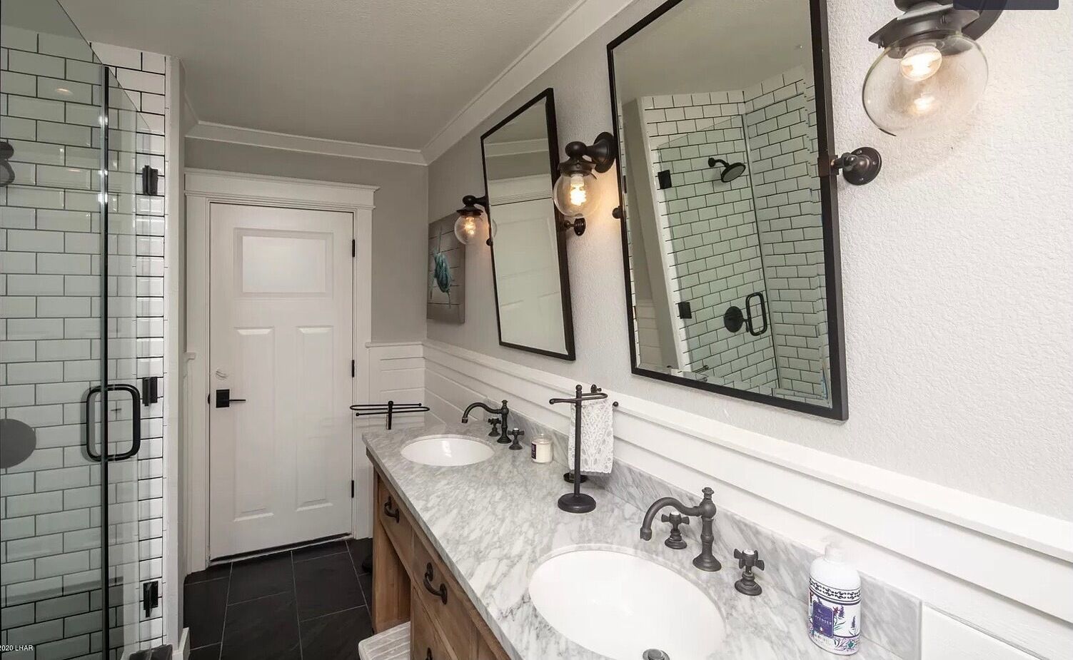 A bathroom with two sinks, a glass shower enclosure, and a white door.