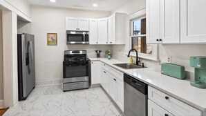 Una cocina moderna con armarios blancos, electrodomésticos de acero inoxidable y piso de mármol.