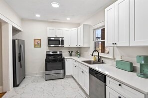 A modern kitchen with white cabinets, stainless steel appliances, and a marble floor. - Atlanta Basecamp | Pet-Friendly | Walkable (Atlanta)
