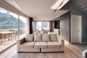 A modern living room with a sofa, dining table, and chairs, large windows with a city view, and a staircase. - Stylish Loft, Balcony and City Views with Parking (Guayaquil)