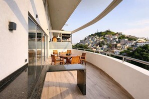 A balcony with a dining table and chairs, a glass door, and a view of a densely packed hillside town. - Stylish Loft, Balcony and City Views with Parking (Guayaquil)