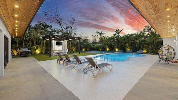A pool area with lounge chairs, a barbecue, and a gazebo under a wooden ceiling. - Villa Solara | Pool · Cinema · Basketball Court  (North Miami Beach)