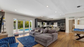 A modern living room with a grey sectional sofa, a pool, a dining area, and a pool table. - Villa Solara | Pool · Cinema · Basketball Court  (North Miami Beach)