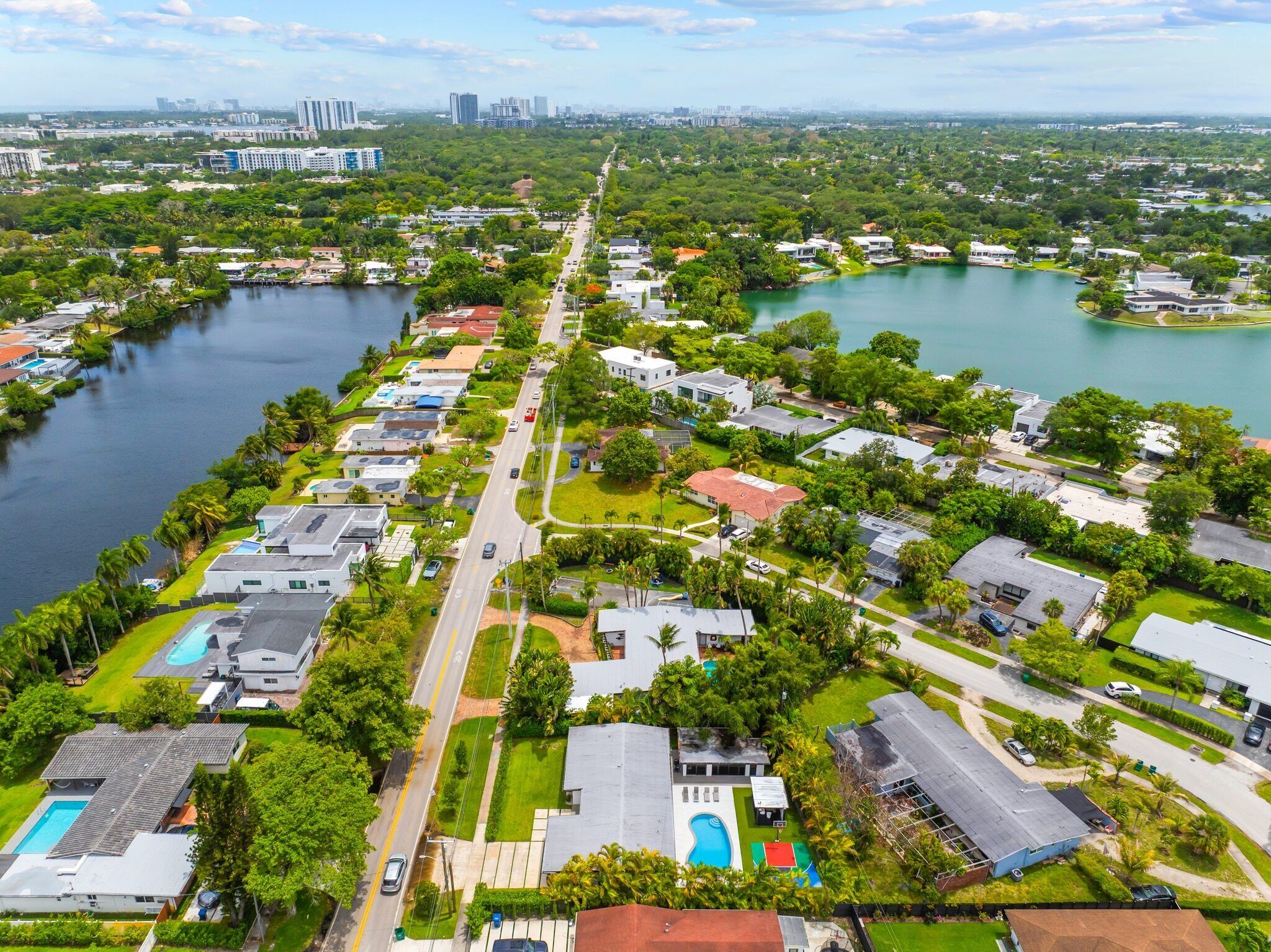 An aerial view of a residential area with houses, a central road, and a lake.