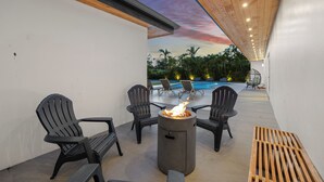 An outdoor seating area with a fire pit, lounge chairs, and a view of a swimming pool. - Villa Solara | Pool · Cinema · Basketball Court  (North Miami Beach)