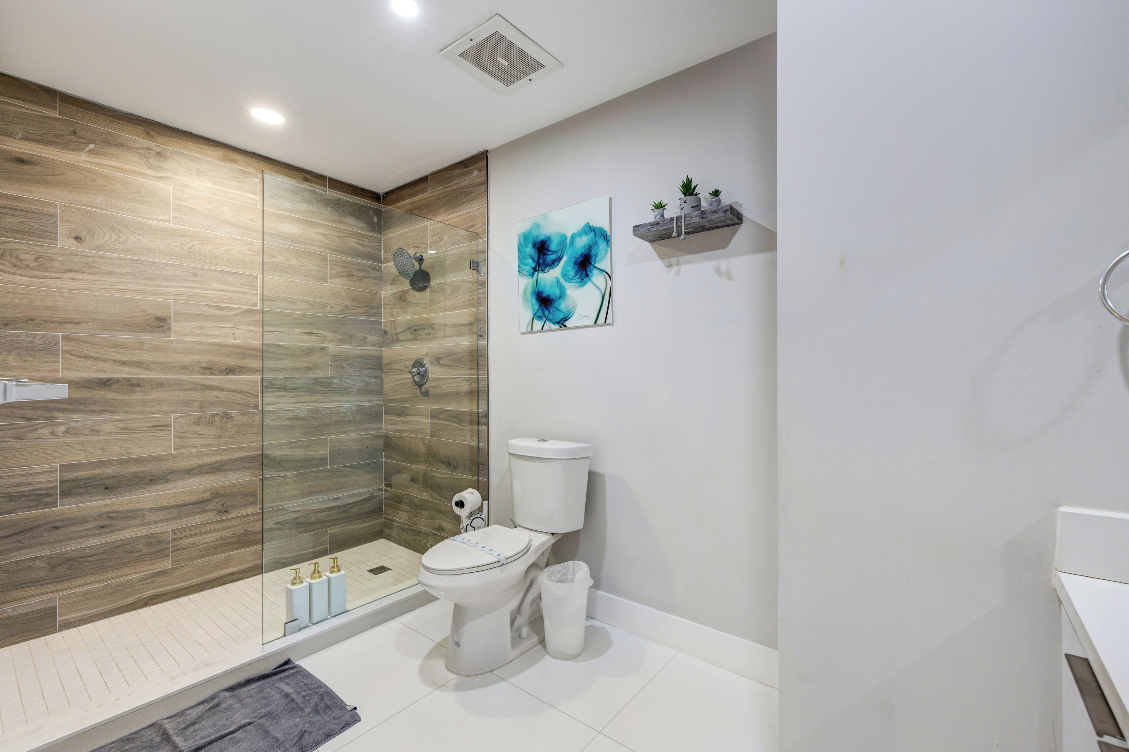 A modern bathroom with a wooden wall, a glass shower enclosure, a toilet, and a sink.