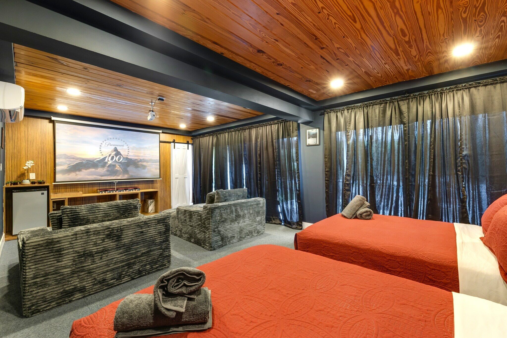 A hotel room with two beds, a TV, a desk, and a large window with curtains.