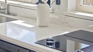 A kitchen with a white marble countertop, a stainless steel sink, a white vase with flowers, and a window with a view of the outside. - Stylish 5BR Entire House Near Vancouver Sleeps 8 Free Parking with AC (Burnaby)