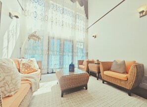 Ein Wohnzimmer mit Korbmöbeln, einem Glastisch und Blick durch große Fenster.