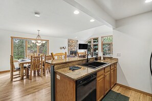 Eine moderne Küche mit einer Granitarbeitsplatte, Holzschränken, einem Geschirrspüler und einem Essbereich mit Holzsesseln und einer Kronleuchter.