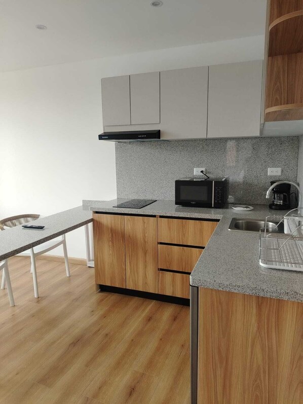 A modern kitchen with a microwave, coffee maker, and wooden cabinets. - ART DECO CUENCA (Cuenca)