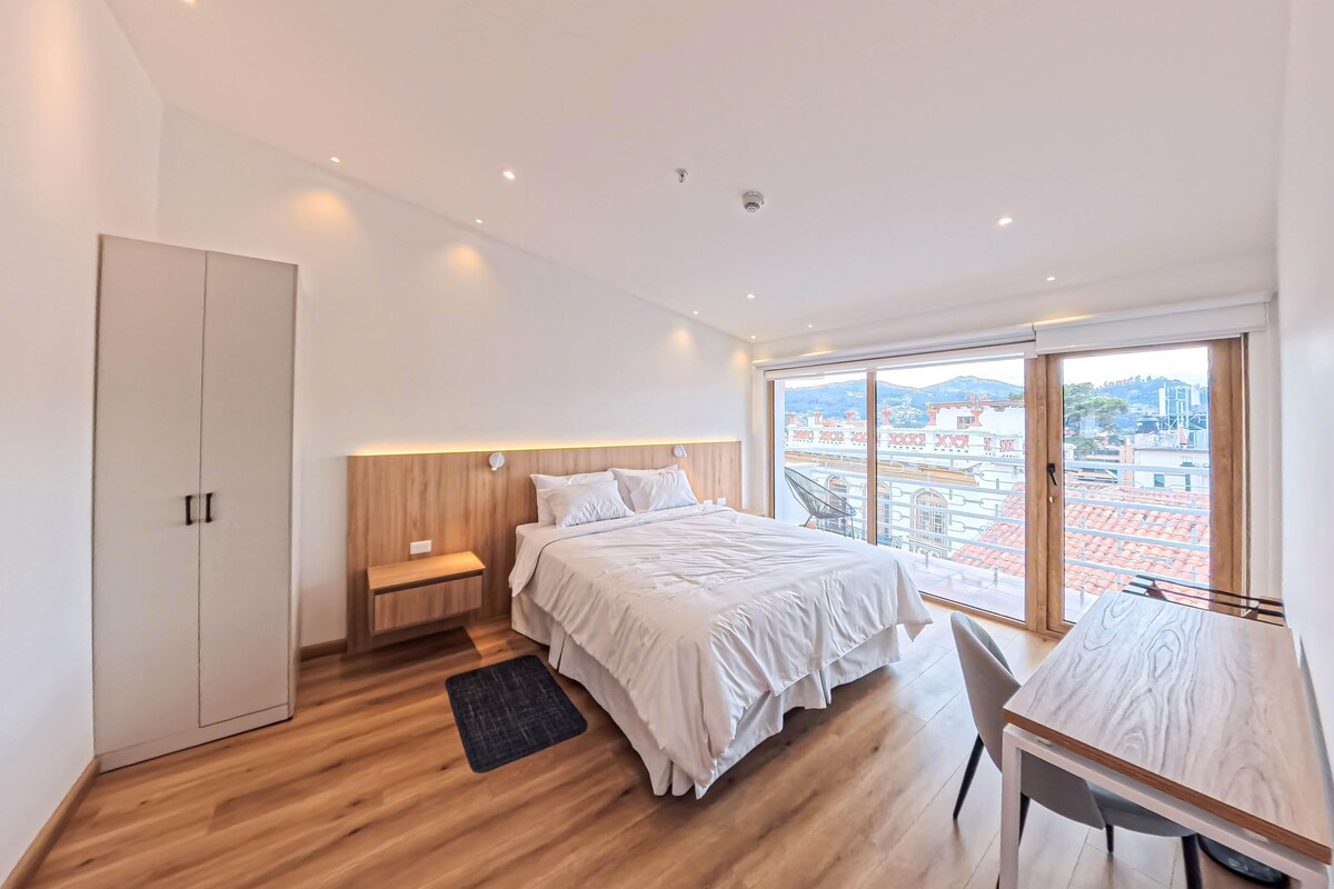A modern bedroom with a large bed, a desk, and a wardrobe.