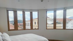 Une chambre à coucher avec un lit, de grandes fenêtres et une vue sur les immeubles.