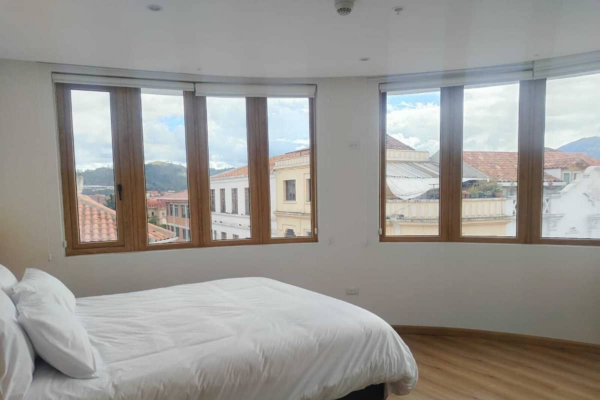 Ein Schlafzimmer mit einem Bett, großen Fenstern und Blick auf Gebäude.