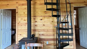 A wooden interior with a spiral staircase, a fireplace, and a dining area. - The Cottage on Robin Hood Lake Off Grid Adventures (Grand Bay-Westfield)