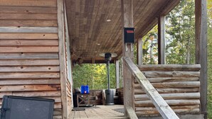 A wooden cabin with a covered porch, a fireplace, and a set of stairs leading to the entrance. - The Cottage on Robin Hood Lake Off Grid Adventures (Grand Bay-Westfield)