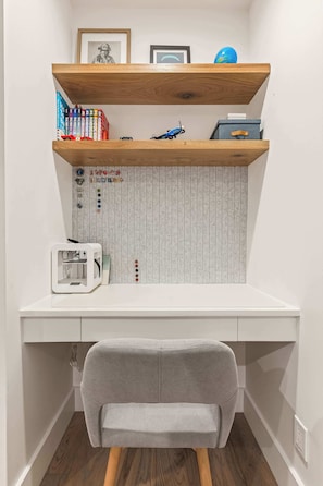 A study area with a white desk, grey chair, wooden shelves, and a patterned wall. - Steps to Sand | Beach Home (Manhattan Beach)