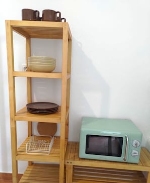 A wooden shelf unit with bowls, plates, and a microwave. - Sintra Refuge (Terrugem)