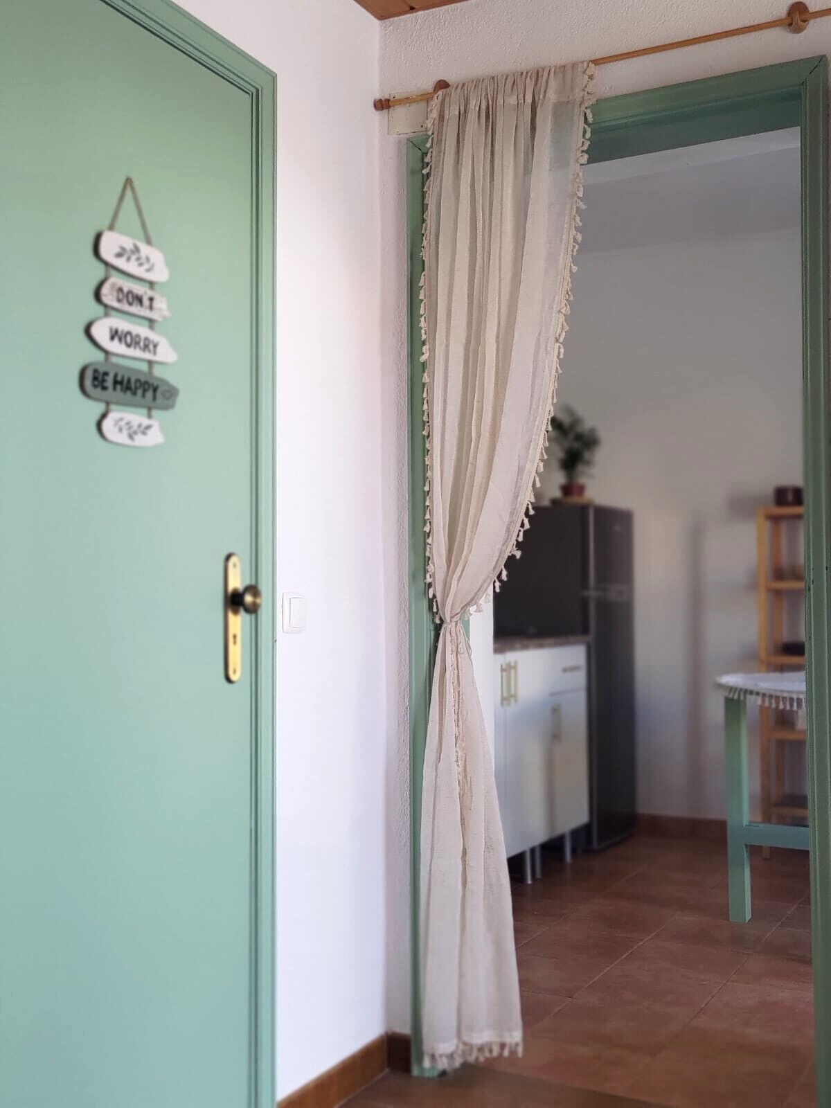 A door with a sign that reads 'DON'T WORRY BE HAPPY,' a curtain, and a glimpse of a kitchen in the background.