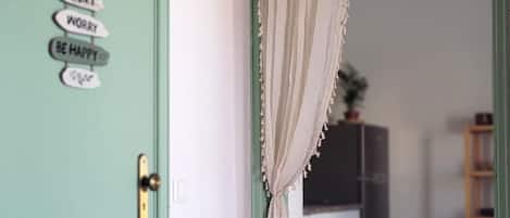 A door with a sign that reads 'DON'T WORRY BE HAPPY,' a curtain, and a glimpse of a kitchen in the background.