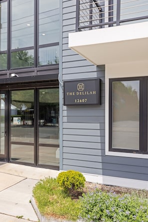 A modern building with a sign reading 'THE DELILAH 12607' and a small garden area with plants.
