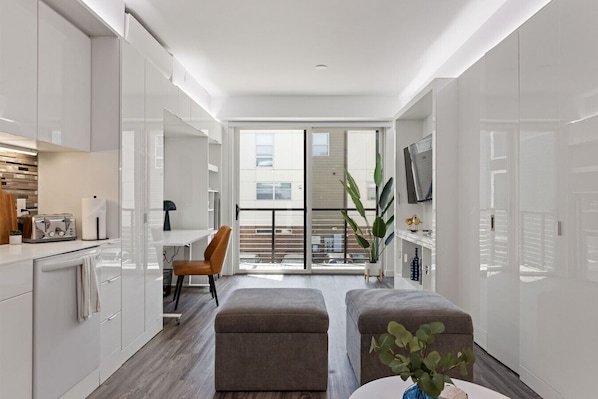 A modern kitchen with white cabinets, a dining area with a chair, and a balcony with a view.