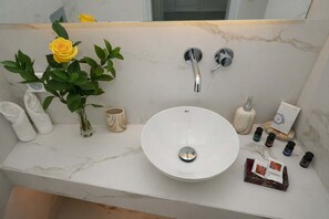 A bathroom with a white marble sink, two faucets, a vase with a yellow rose, and toiletries. - Iliana s Getaway - Private Villa With Jacuzzi (Santorini)