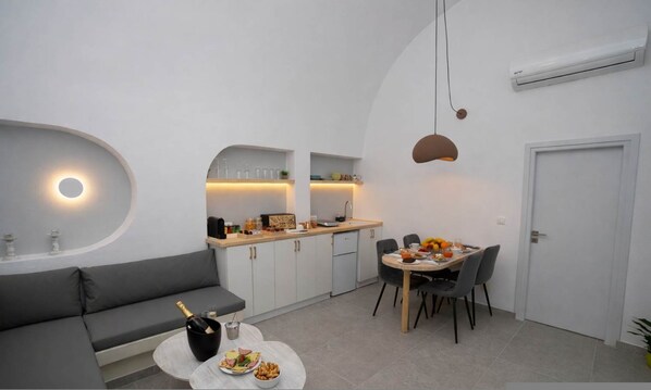 A modern kitchen with a dining area, a built-in oven, and a seating area with a sofa and table. - Iliana s Getaway - Private Villa With Jacuzzi (Santorini)