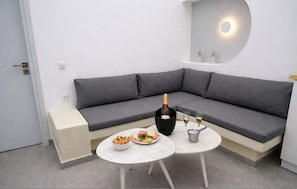 A modern living area with a grey sofa, a small round table with snacks and a bottle of champagne, and a wall-mounted light fixture. - Iliana s Getaway - Private Villa With Jacuzzi (Santorini)