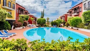 Una piscina con sillones de descanso, rodeada de edificios con balcones y vegetación.